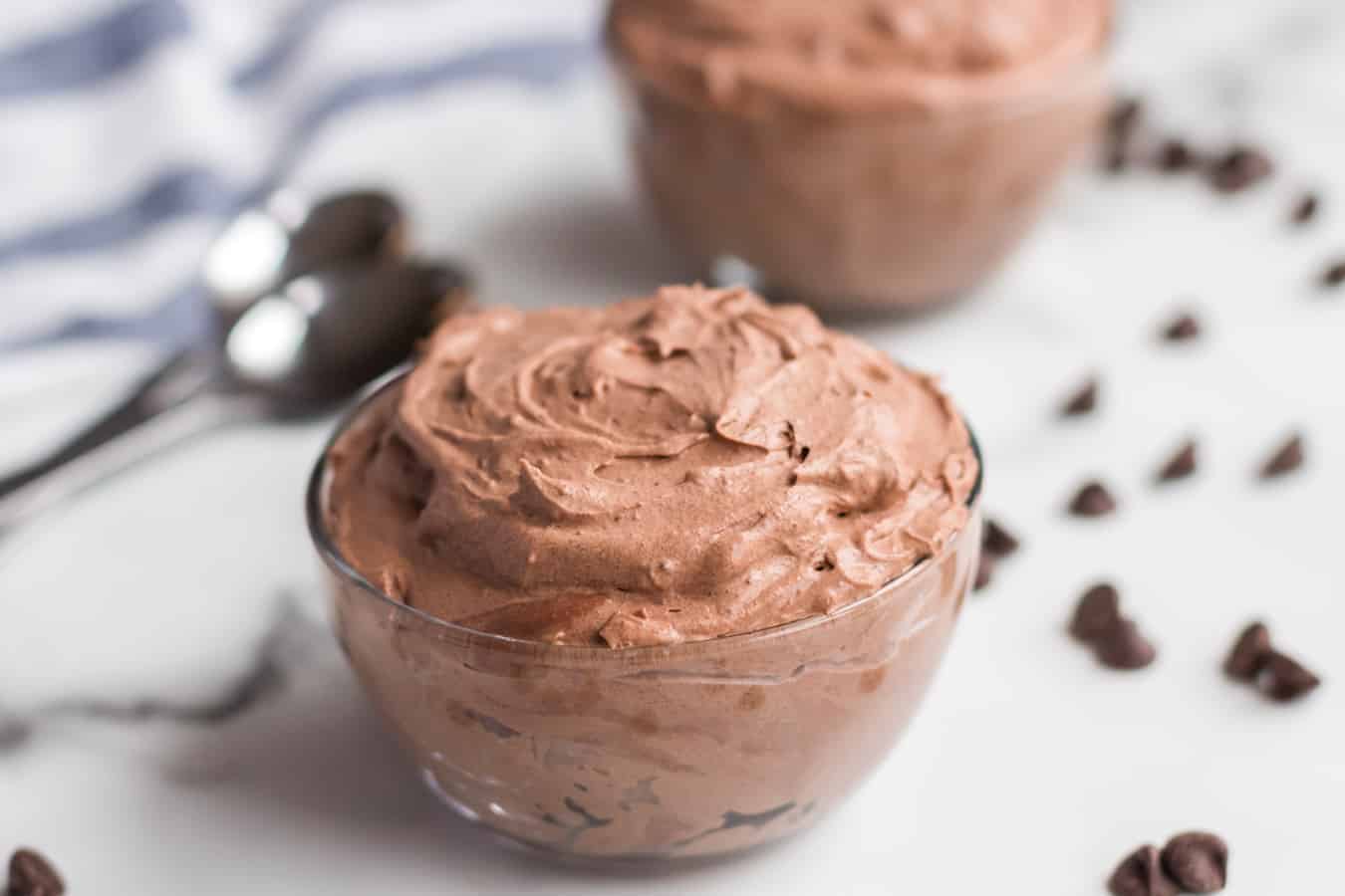 Small glass serving bowl filled with chocolate mousse and there are two spoons and another small bowl of mousse in the background. 