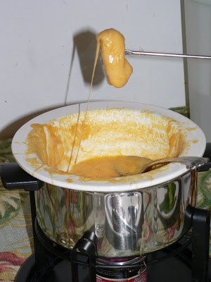 A square of bread being dipped in cheese fondue in a metal fondue pot