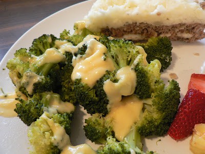 A white plate with broccoli florets drizzled with cheese sauce