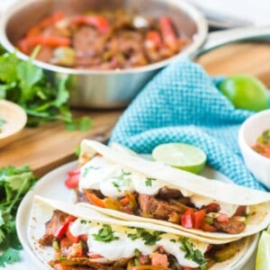 flour tortillas with steak and peppers with lime on a white plate with fajita mix in the background