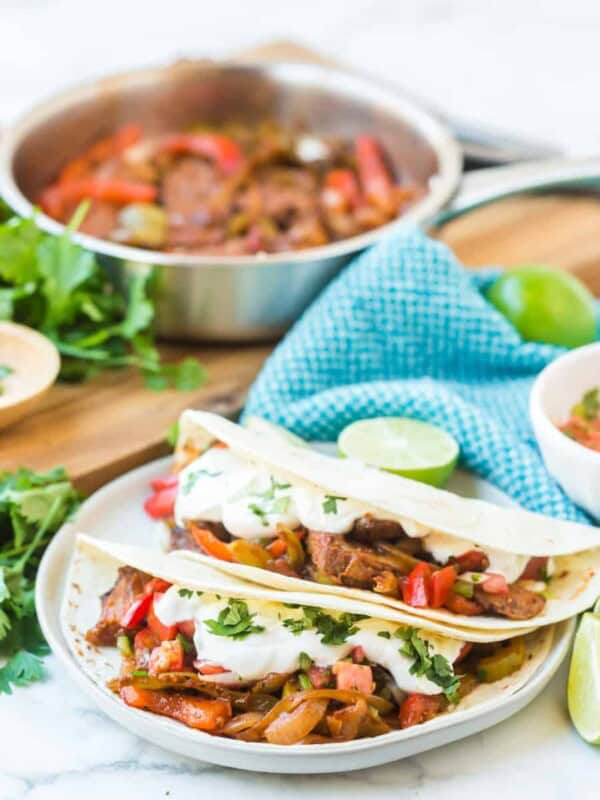 flour tortillas with steak and peppers with lime on a white plate with fajita mix in the background