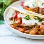 close up of fajita with steak and onions and peppers and sour cream in a flour tortilla on a white plate