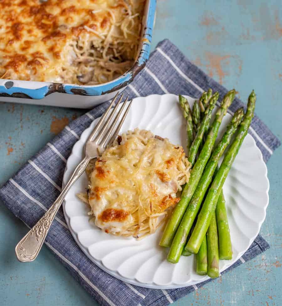 Dished chicken tetrazzini on a plate with a side of asparagus ready to dig into. 