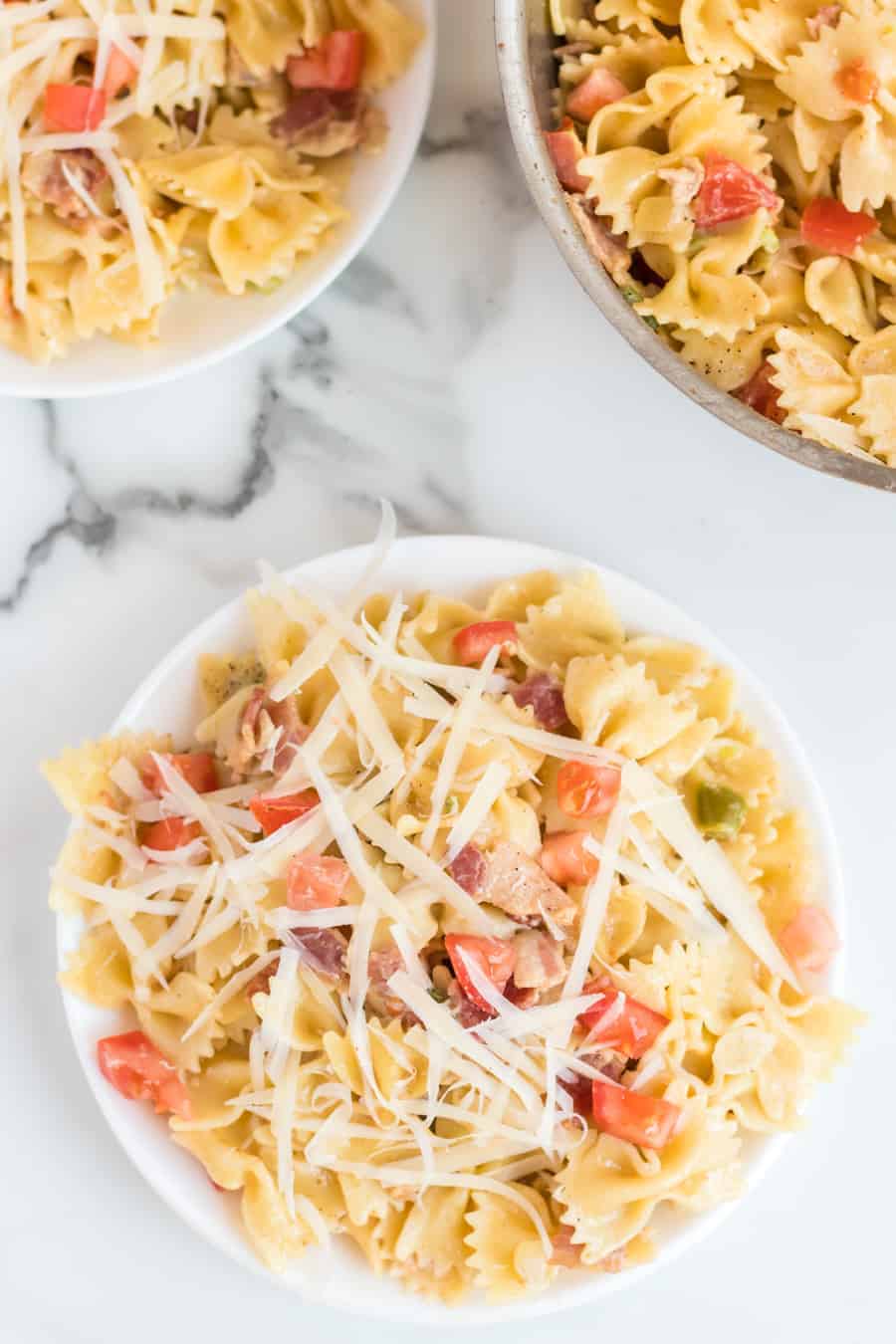 Bowtie pasta in a bowl with chunks of tomato, a light cream sauce, and shredded Parmesan cheese on top. 