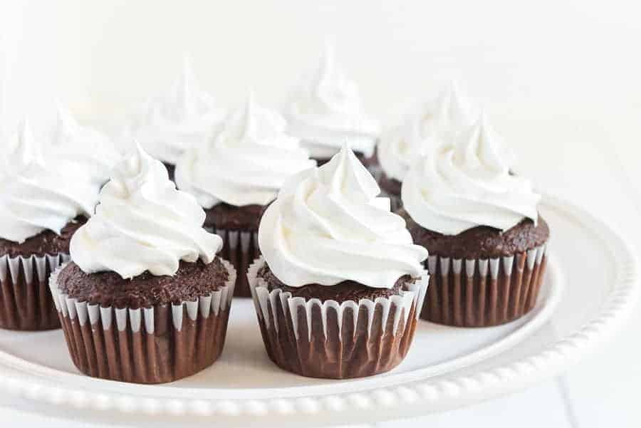 close up image of chocolate cupcakes with white frosting on a white plate.