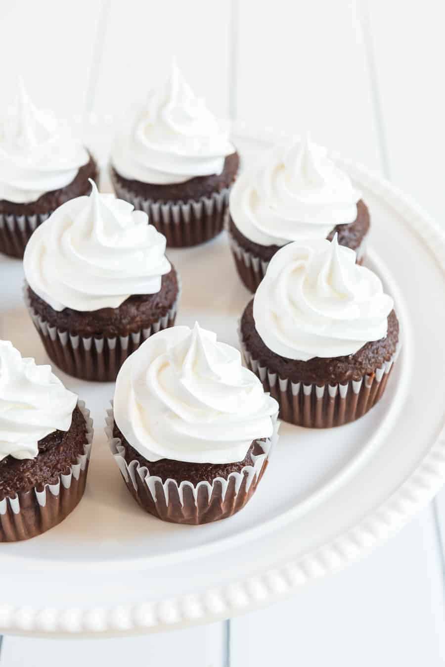 close up image of chocolate cupcakes with white frosting on a white plate.