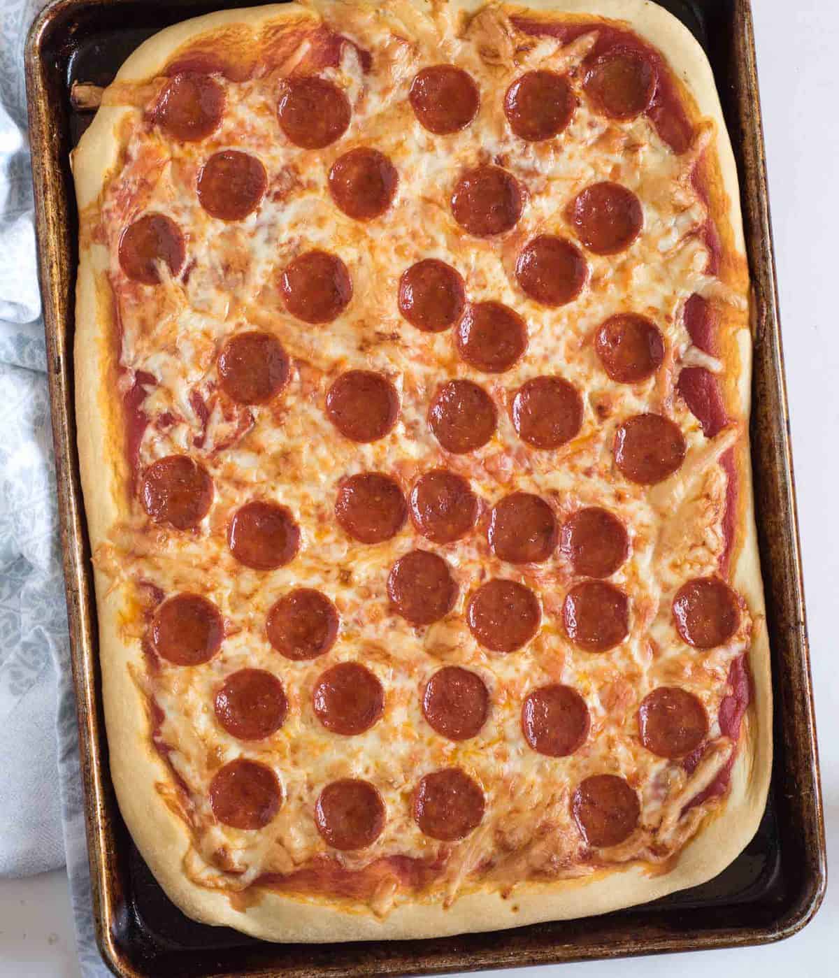 The best easy pizza dough recipes is made with only 6 simple ingredients and comes together in about 10 minutes. We use this dough for everything from traditional pizza to bread sticks and more! Top view of a cheese and pepperoni pizza on a sheet pan.