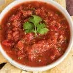 blue and yellow corn tortilla chips around a small white bowl of red salsa