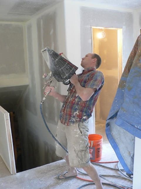 A man holding a triangular-shaped tool with a hose to add wall texture