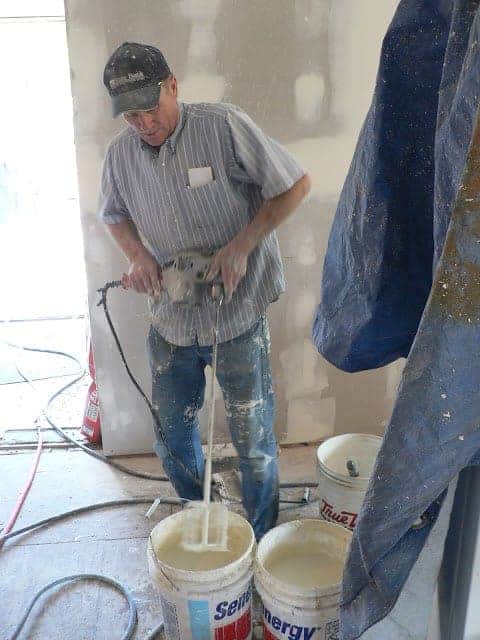 A man using a mixing tool in a bucket of white wall paste mixture