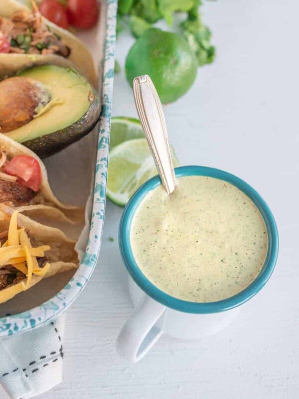 A bowl of creamy cilantro ranch dressing next to a pan of tacos.