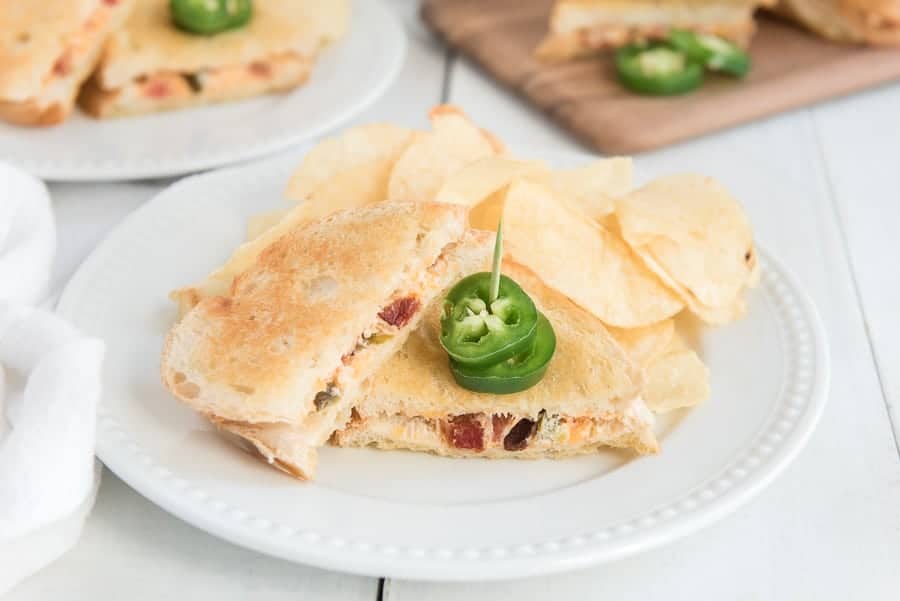 jalapeno grilled cheese on white plate with jalapenos on toothpick and a side of potato chips