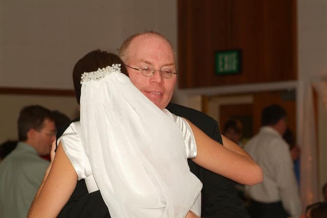 Back view of a bride with a veil hugging her father