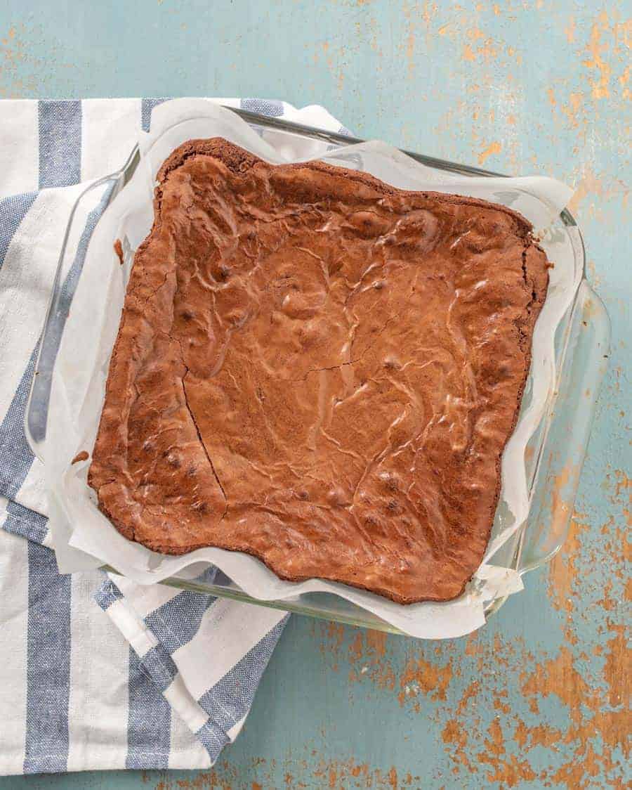 A whole pan of baked brownies in the pan sitting on a white-and-blue striped towel.