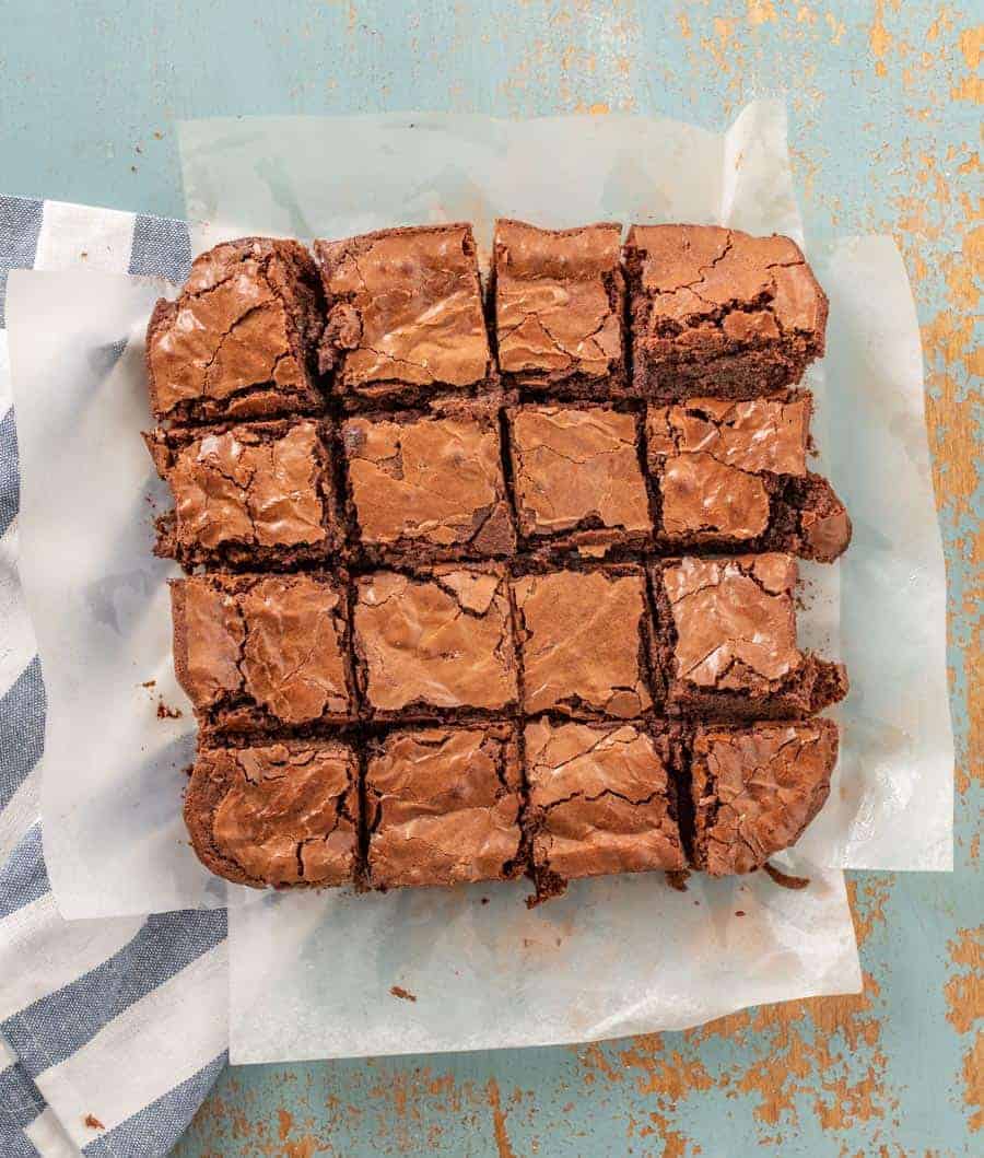 A pan of brownies cut into 16 on a piece of white parchment paper. 