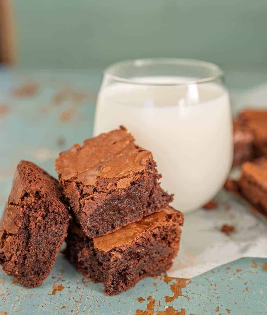 Three brownies with a glass of milk in the background. 