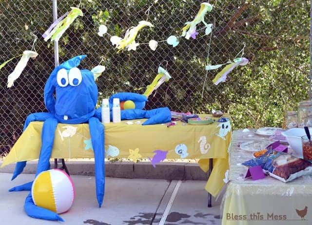 A giant blue hand-made octopus on a party table with yellow tablecloth and beach-themed decorations