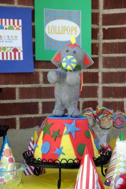 An elephant birthday cake surrounded by a table of circus-themed decorations