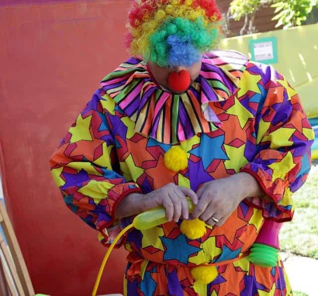 A person in a colorful clown costume making balloon animals