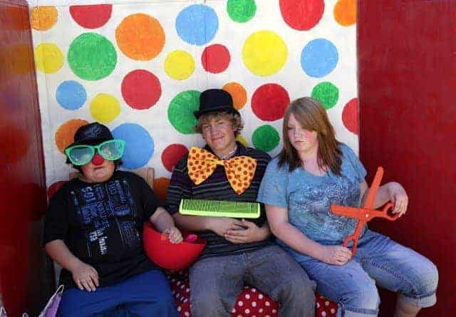Three people in a circus-themed photo booth with props and a polka dotted wall backdrop