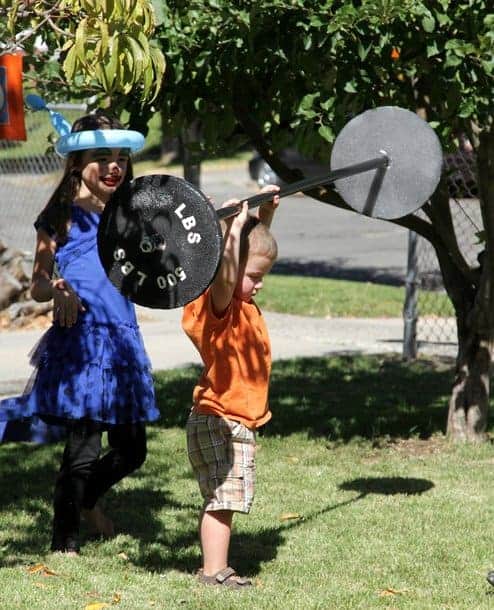 A little boy holding up a pretend 500-lb weight barbell