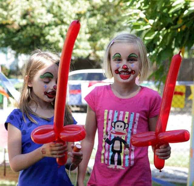Two girls with clown face paint and red balloon swords