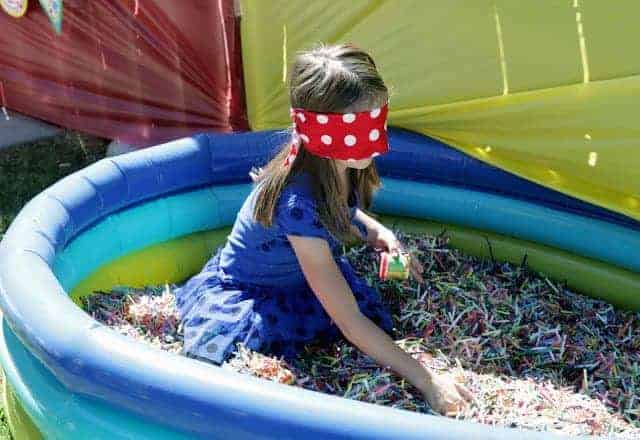 A little girl with a blindfold in an inflatable pool filled with shredded paper