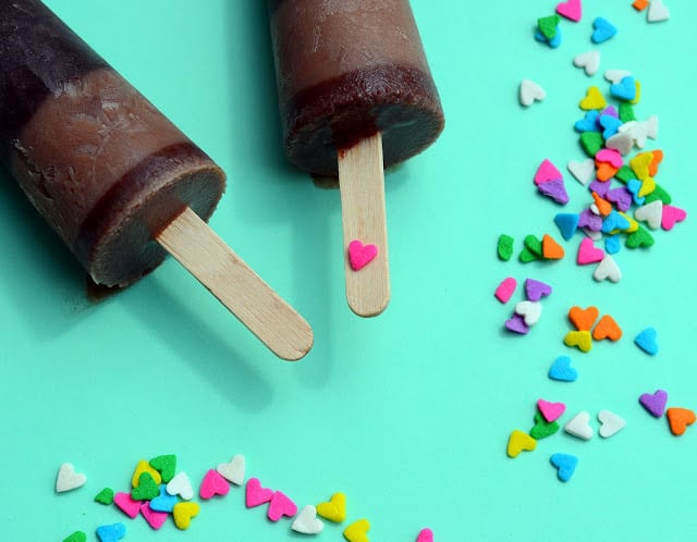 Two fudge pops laying on an aqua background surrounded with heart-shaped sprinkles 