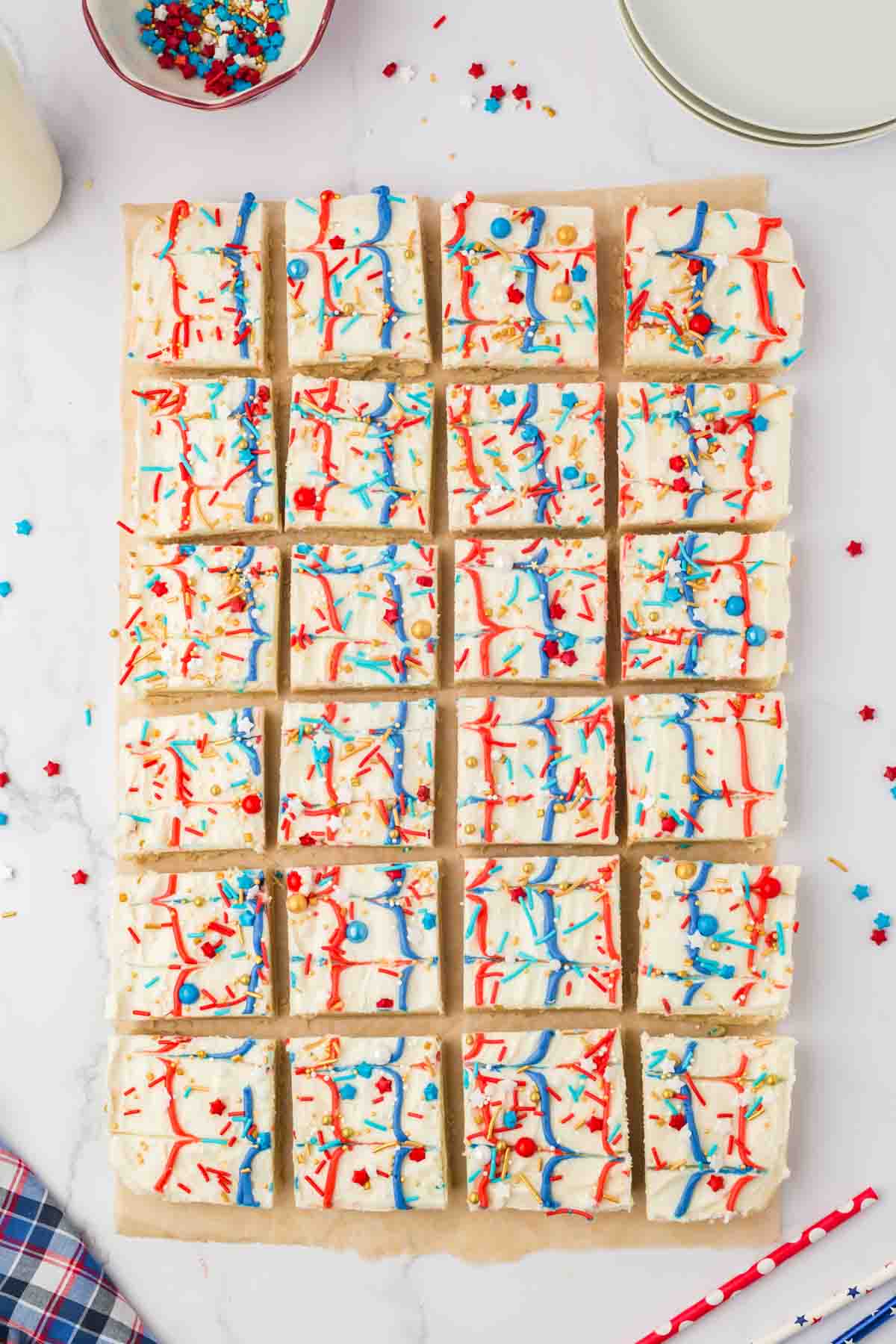 top view of red white and blue iced sugar cookie bars with star shaped sprinkles on wax paper