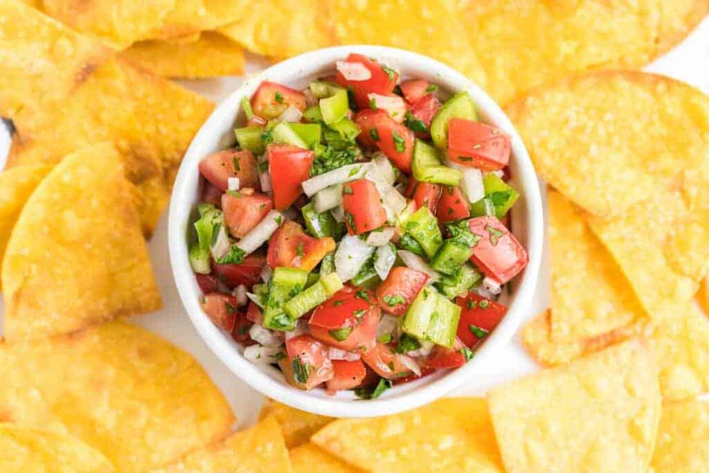 chunky fresh salsa in a white dish with tortilla chips all around