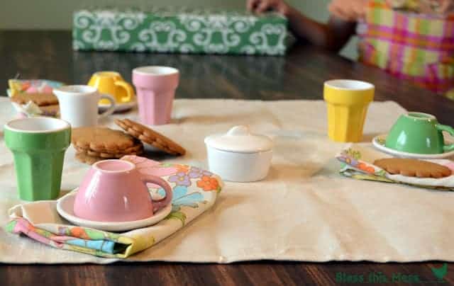 A colorful tea set on a table with floral cloth napkins and cookies