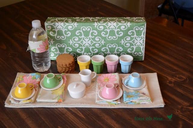 A green and white decorative box with a colorful tea set, napkins and cookies displayed in front