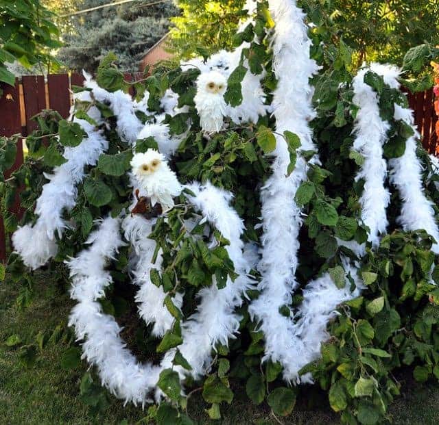 White feather boas and white stuffed owls in a shrub