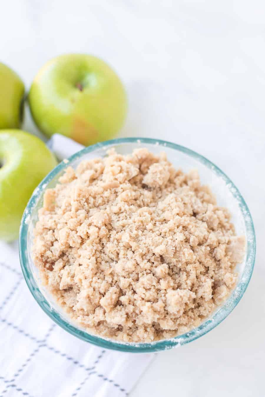 crumble mixture in a bowl with green apples in the background.