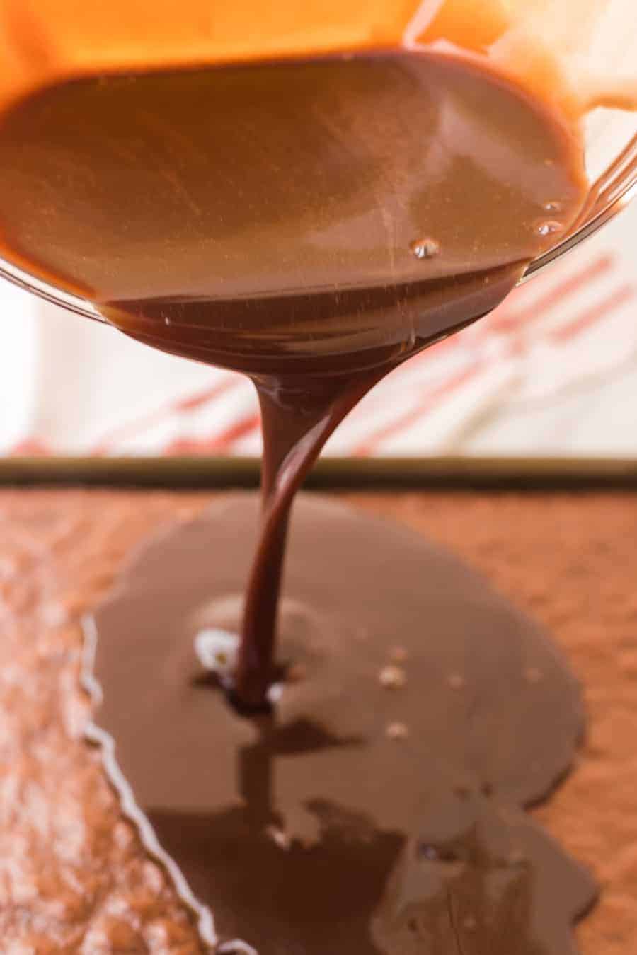 chocolate icing being poured onto chocolate sheet cake.