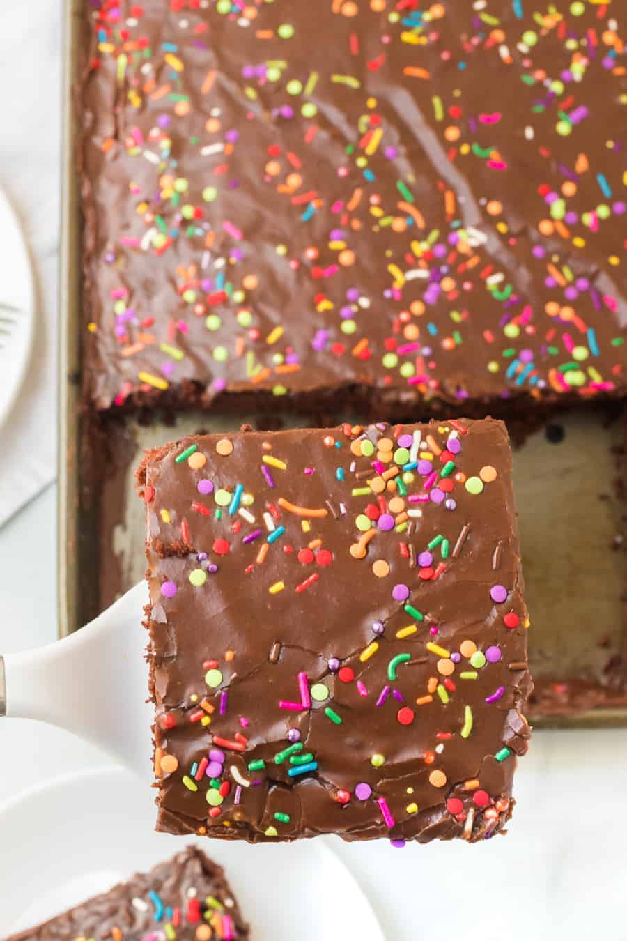 chocolate sheet cake with colored sprinkles in metal rectangle pan with one slice being taken out.