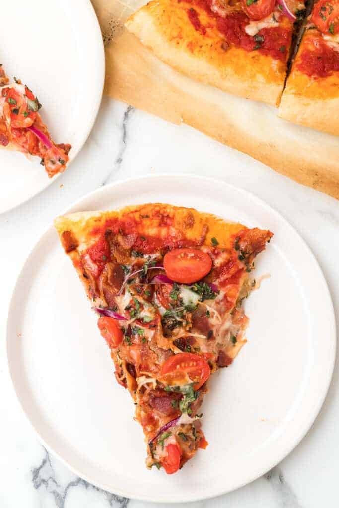 a slice of herbed tomato and bacon pizza on a white plate