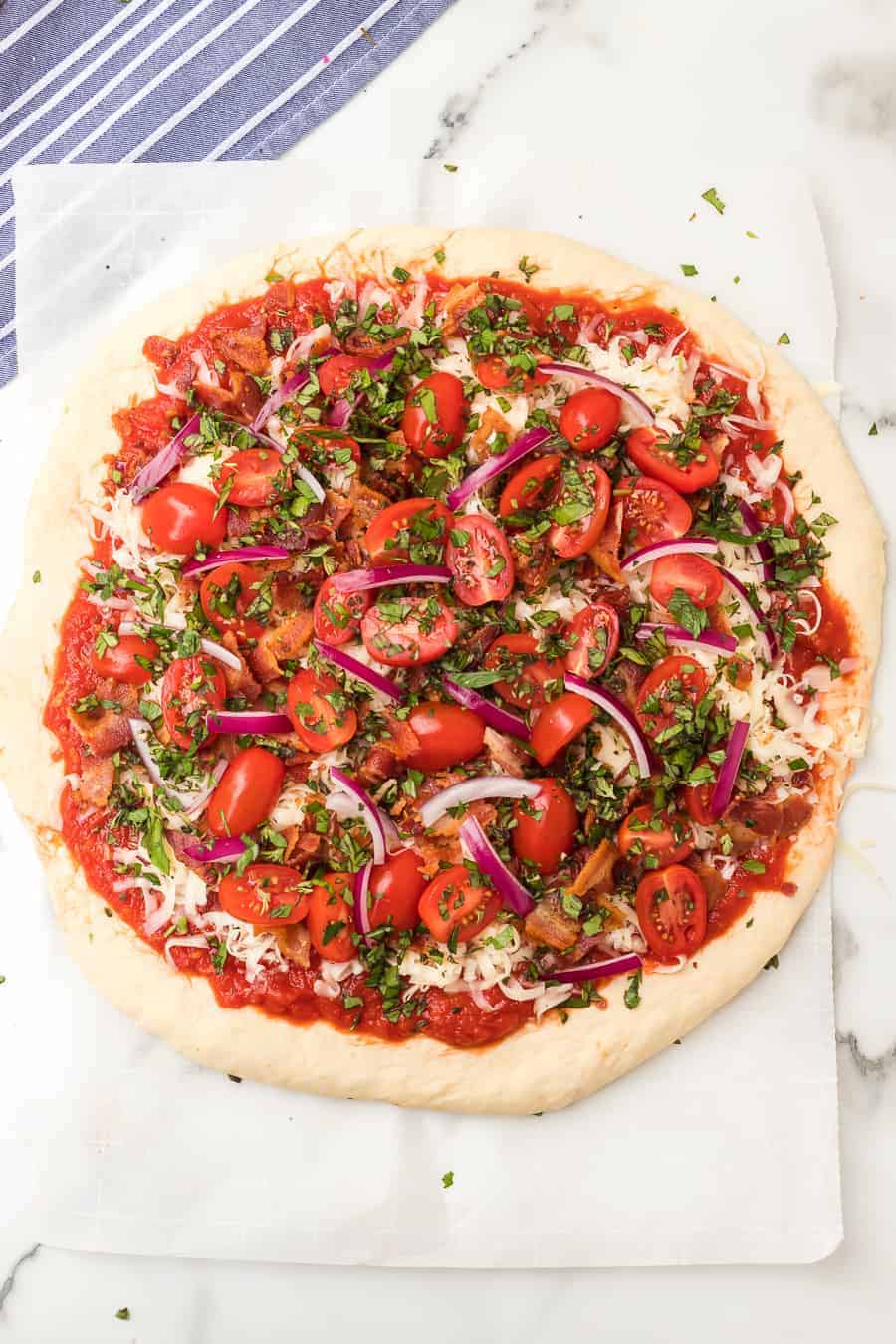 Homemade pizza dough topped with bacon, cheese, tomatoes, and herbs is the perfect pizza to make tonight. Your whole family will love it! #pizza #homemadepizza #tomatobaconpizza