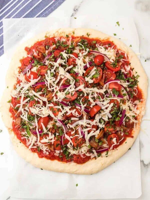 a raw a whole herbed tomato and bacon pizza on parchment