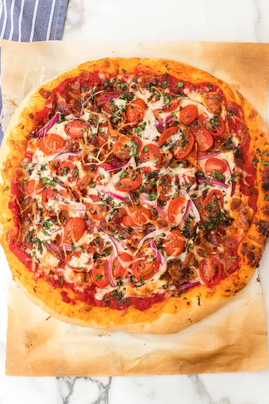 Homemade pizza dough topped with bacon, cheese, tomatoes, and herbs is the perfect pizza to make tonight. Your whole family will love it! #pizza #homemadepizza #tomatobaconpizza