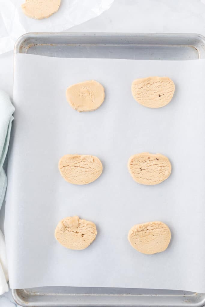 a baking sheet and white parchment of six pieces of cookie dough