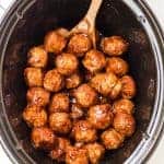 top view of slow cooker with teriyaki meatballs in it and a wooden spoon