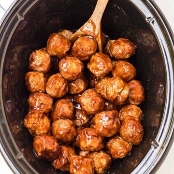 top view of slow cooker with teriyaki meatballs in it and a wooden spoon
