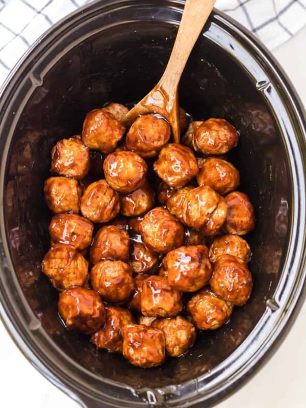 top view of slow cooker with teriyaki meatballs in it and a wooden spoon