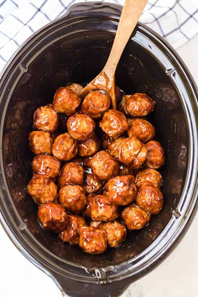top view of slow cooker with teriyaki meatballs in it and a wooden spoon