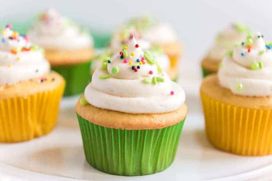 A cupcake that has been iced and sprinkled is in the foreground with other decorated cupcakes in the background.