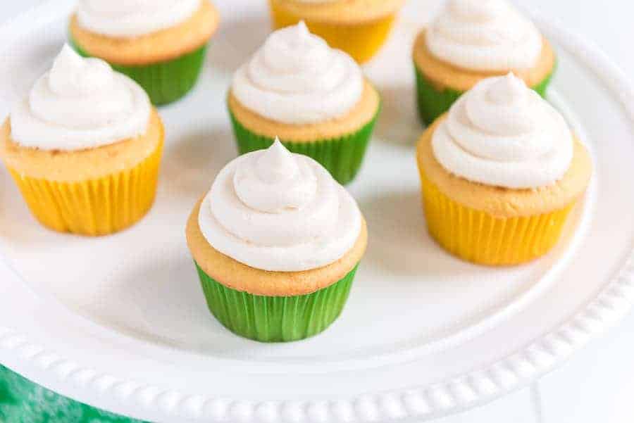 An iced cupcake is shown in the foreground with six other cupcakes in the background on an elegant white plate.