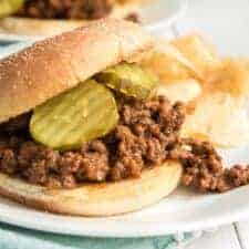 sloppy joe on a plate with pickles and chips