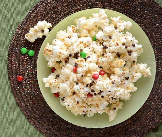 The best gooey Marshmallow Christmas Popcorn with Chocolate is a treat that your whole family will love! popcorn in a large green bowl on a brown placemat