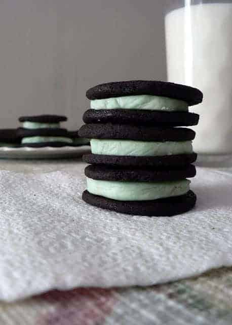 stack of three homemade mint oreo cookies with dark chocolate outside and mint green inside stacked on a white towel with a clear glass of white milk behind.